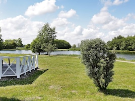 Un parque con una pasarela de madera, un árbol pequeño y un lago.