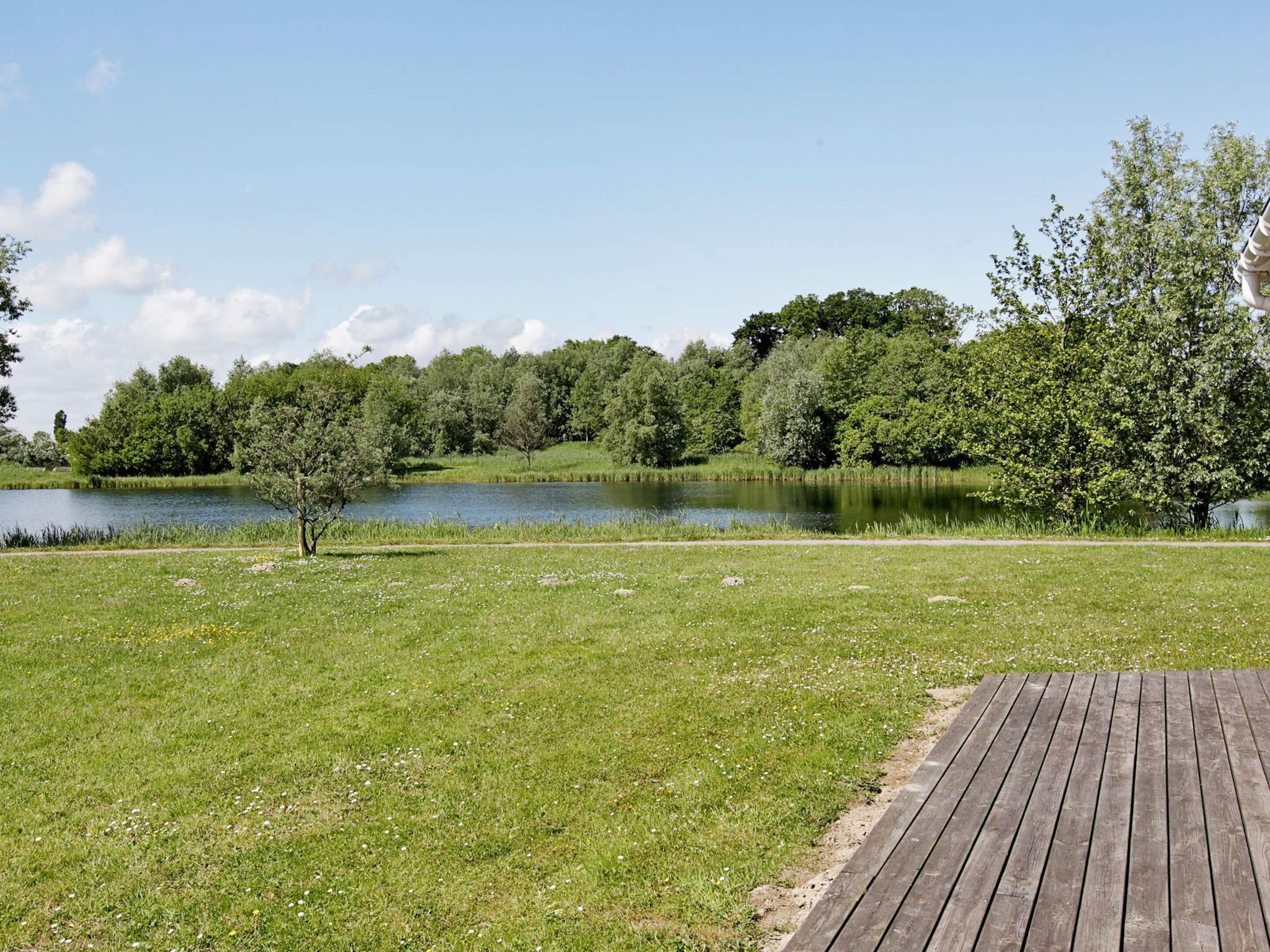A grassy area with a wooden deck and a lake surrounded by trees.