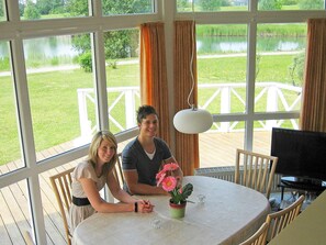 A room with a large window, a dining table, and a television. - Holiday Home in Otterndorf (Otterndorf)