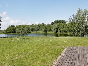 Eine grüne Wiese mit einer Holzterrasse und einem von Bäumen umgebenen See.