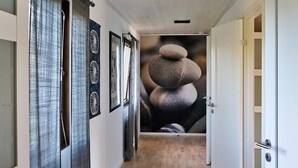 Un couloir doté d’un plancher en bois, une porte sur la droite et un mur orné d’une fresque représentant un empilement de roches.
