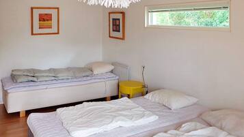 A bedroom with two beds, a radiator, a small yellow table, and two framed pictures on the wall.