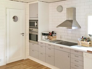 Una cocina con puerta blanca, electrodomésticos de acero inoxidable, salpicadero de azulejos blancos y encimera de madera.
