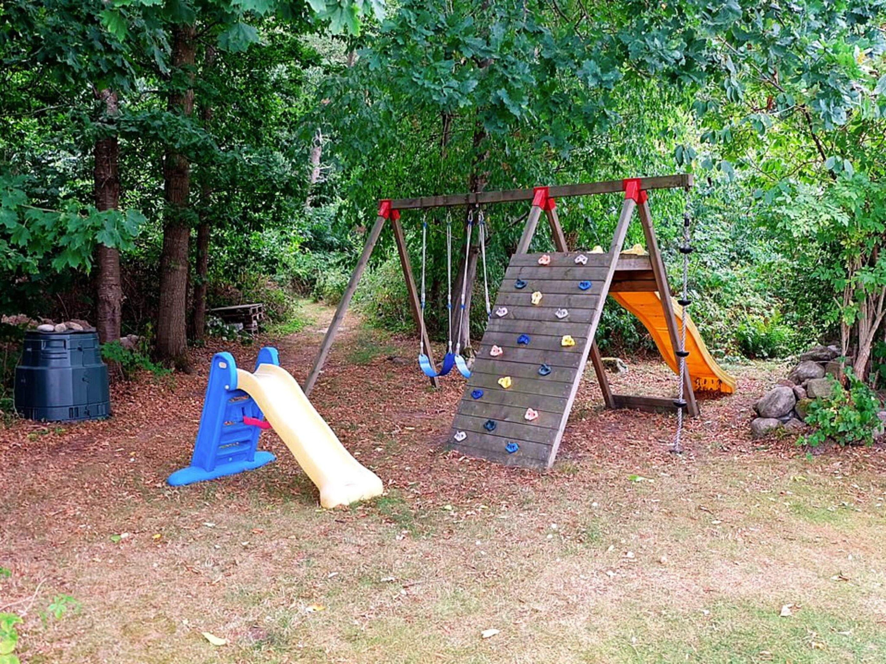 A playground with a slide, climbing wall, and swing set surrounded by trees.