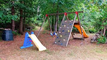 A playground with a slide, climbing wall, and swing set surrounded by trees.