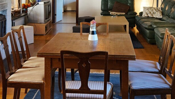 Un coin repas avec une table et des chaises en bois, un téléviseur en arrière-plan et un canapé avec des coussins.