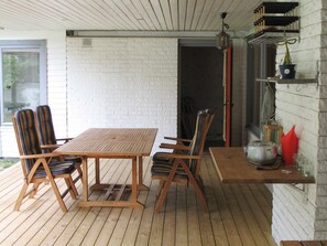 Una terraza de madera con una mesa y sillas, un muro de ladrillo y un aplique colgante.