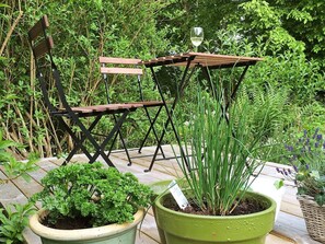 Un jardín con un banco de madera, una planta en maceta y una mesa con una copa de vino blanco.