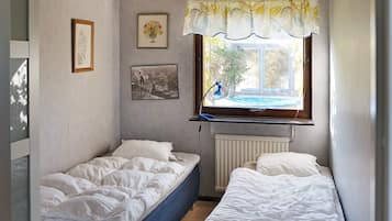 Et lille soveværelse med to senge, en radiator, et vindue med udsigt, og billedkunst på væggene.