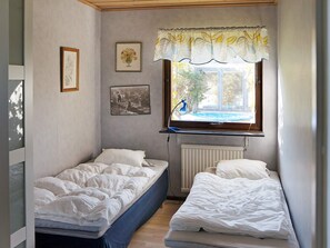 Un dormitorio pequeño con dos camas individuales, un radiador, un ventanal con vistas al exterior y decoración en las paredes.