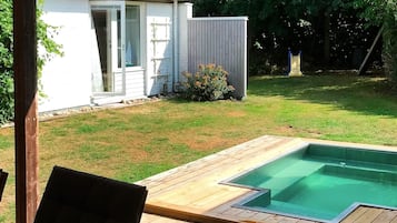 A backyard with a swimming pool, a wooden deck, and a white house.