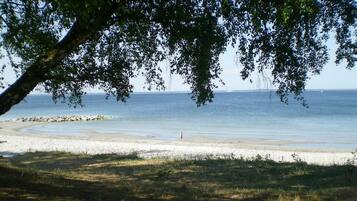 A beach with a clear view of the sea, a sandy shore, and a person walking.