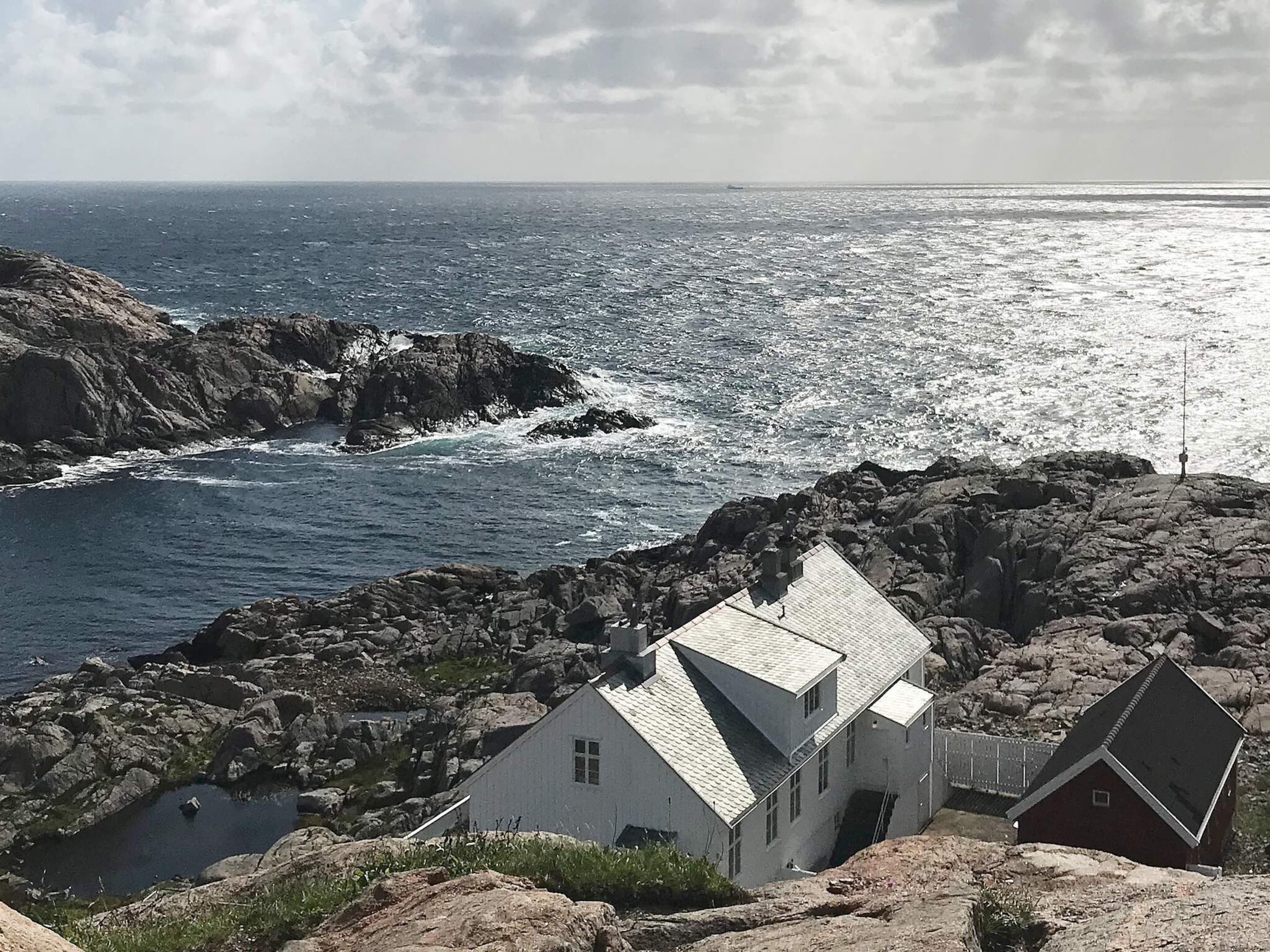 A coastal house with a steep roof, situated on rocky terrain with a view of the ocean.