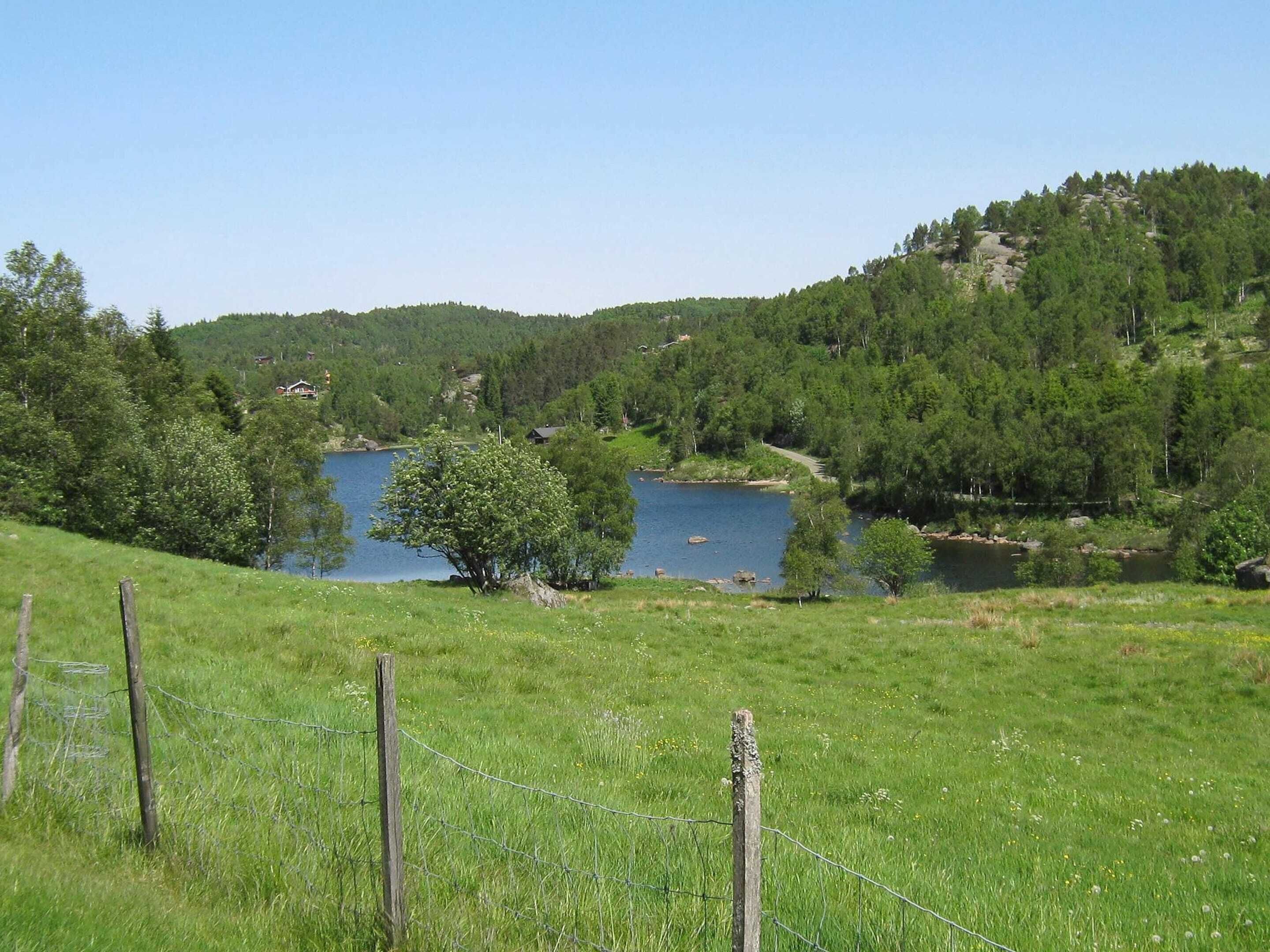 Paisatge rural amb un llac, envoltat de vegetació i turons.
