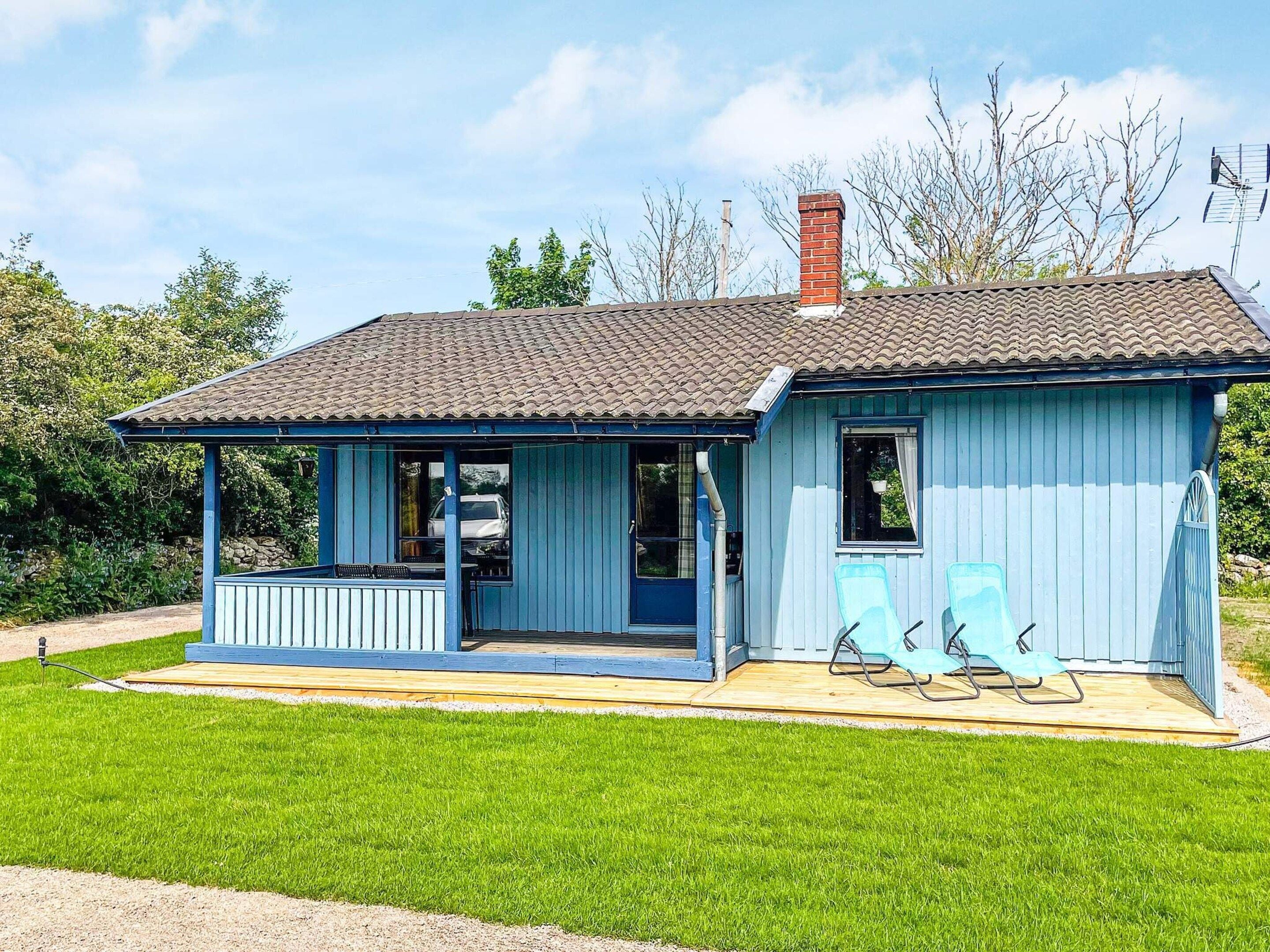 A small, single-story building with a porch and two outdoor chairs.