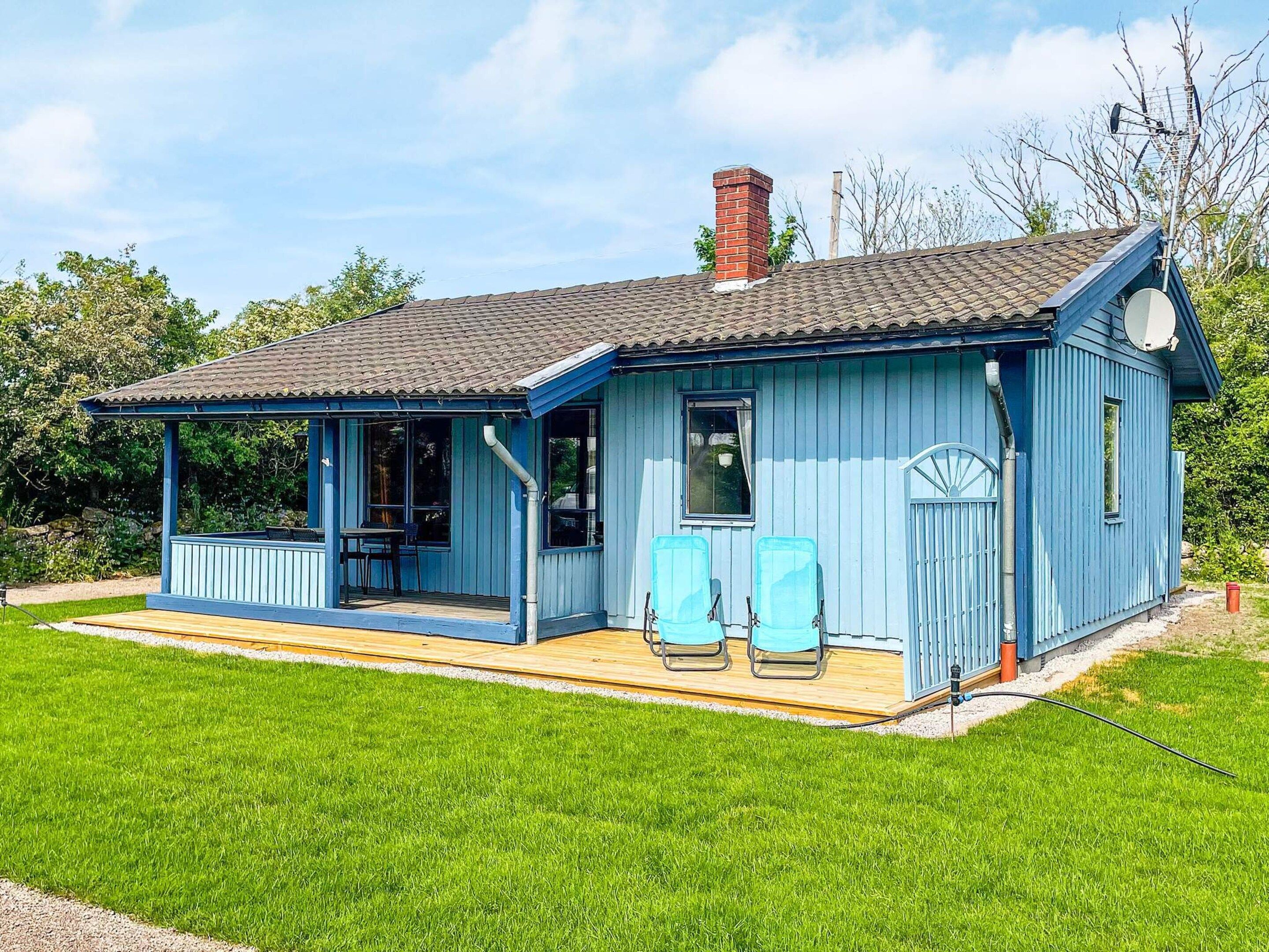A blue wooden house with a porch, two chairs, and a chimney.