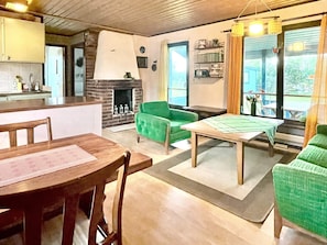 A cozy living area with a fireplace, green armchairs, a dining table, and a view of the outdoors. - 4 Star Holiday Home in Kopingsvik (Kopingsvik)