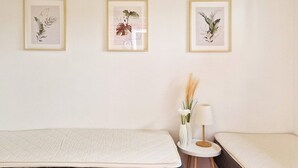 A bedroom with two beds, a small round table with a lamp, and three framed botanical prints on the wall. - 6 Person Holiday Home in Gudhjem (Gudhjem)