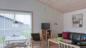 Un salon moderne comprenant un coin repas, des meubles en bois, un téléviseur et une vue sur l’extérieur.