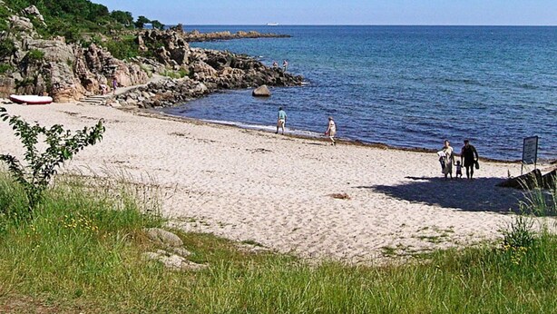Une plage de sable avec des affleurements rocheux et une mer d’un bleu limpide.