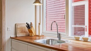 Une cuisine dotée d’un évier en acier inoxydable, d’un plan de travail en bois et d’une fenêtre avec un revêtement extérieur rouge.