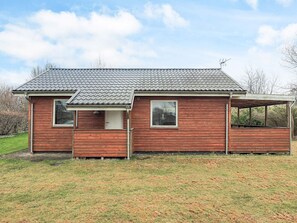 A single-story wooden house with a tiled roof, a covered porch, and a small attached shed.