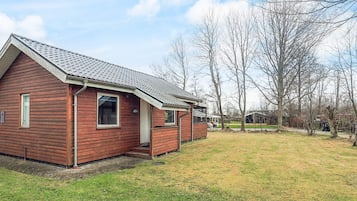 A red wooden cabin with a sloped roof, a small porch, and a grassy yard.