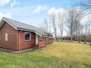Une cabane en bois rouge, avec un toit en pente, un petit porche et une cour couverte d’herbe.