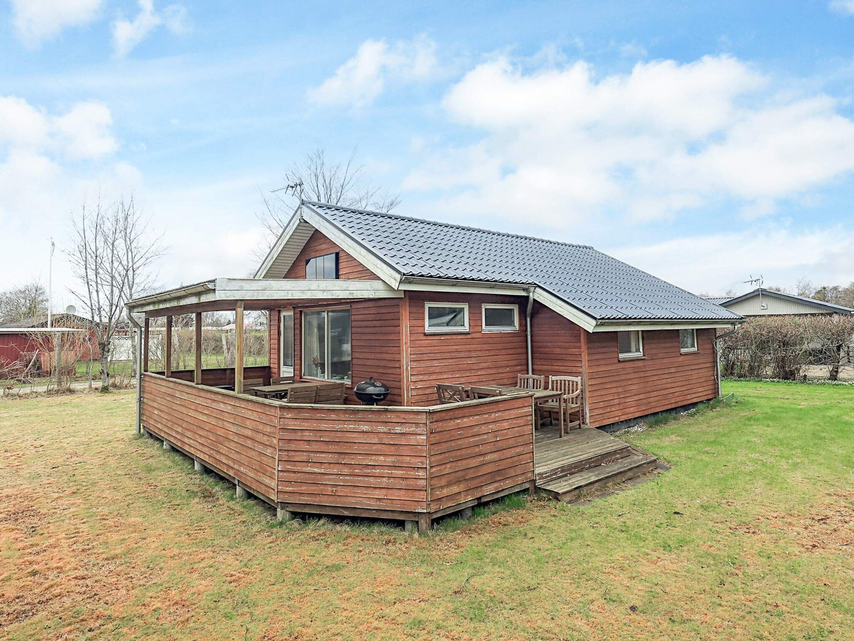 A wooden house with a covered patio, a barbecue grill, and a small deck.