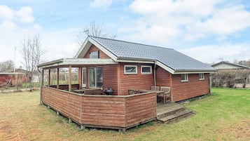 A wooden house with a covered patio, a barbecue grill, and a small deck.