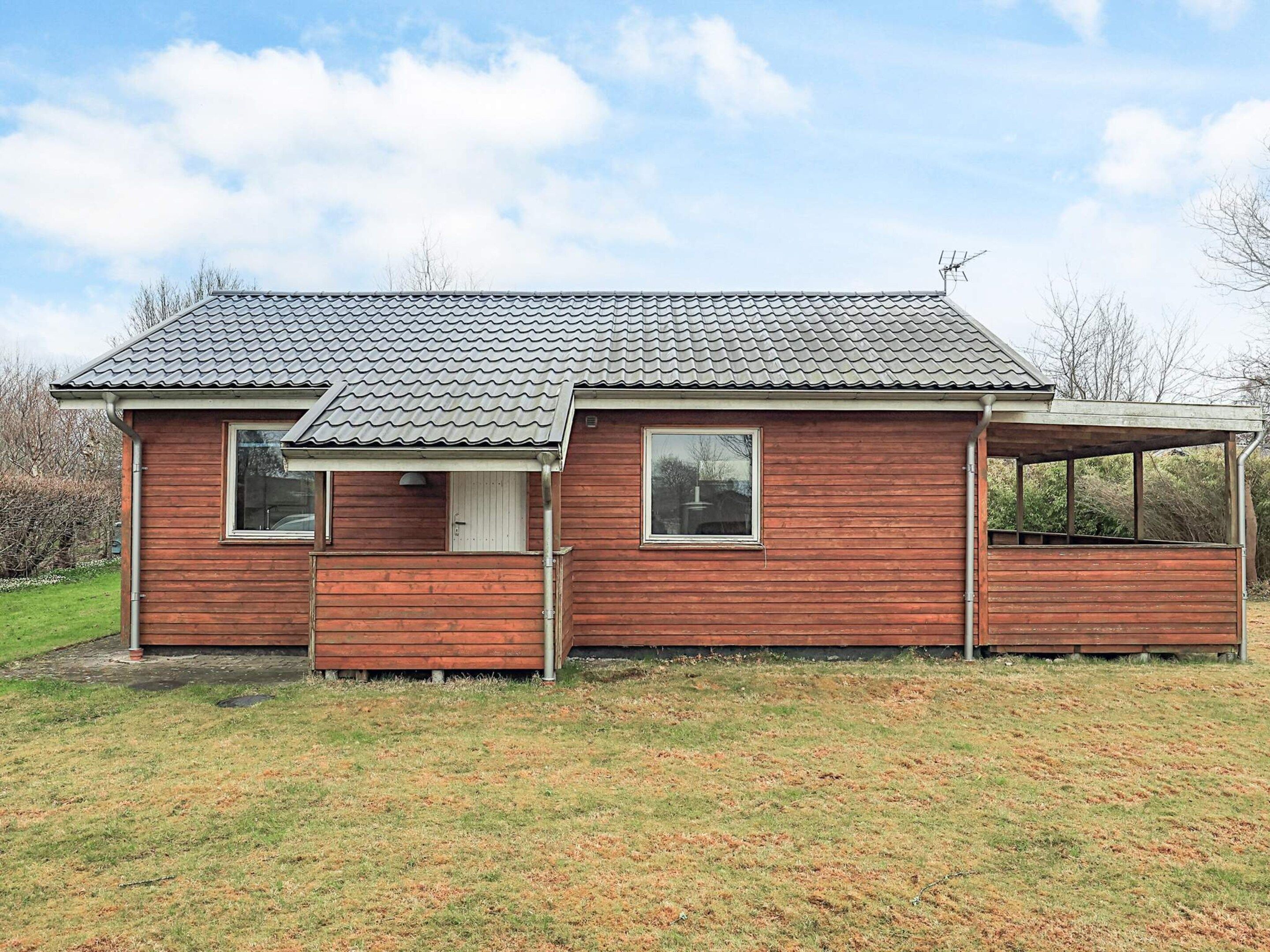 A single-story wooden house with a tiled roof, a porch, and a covered area.