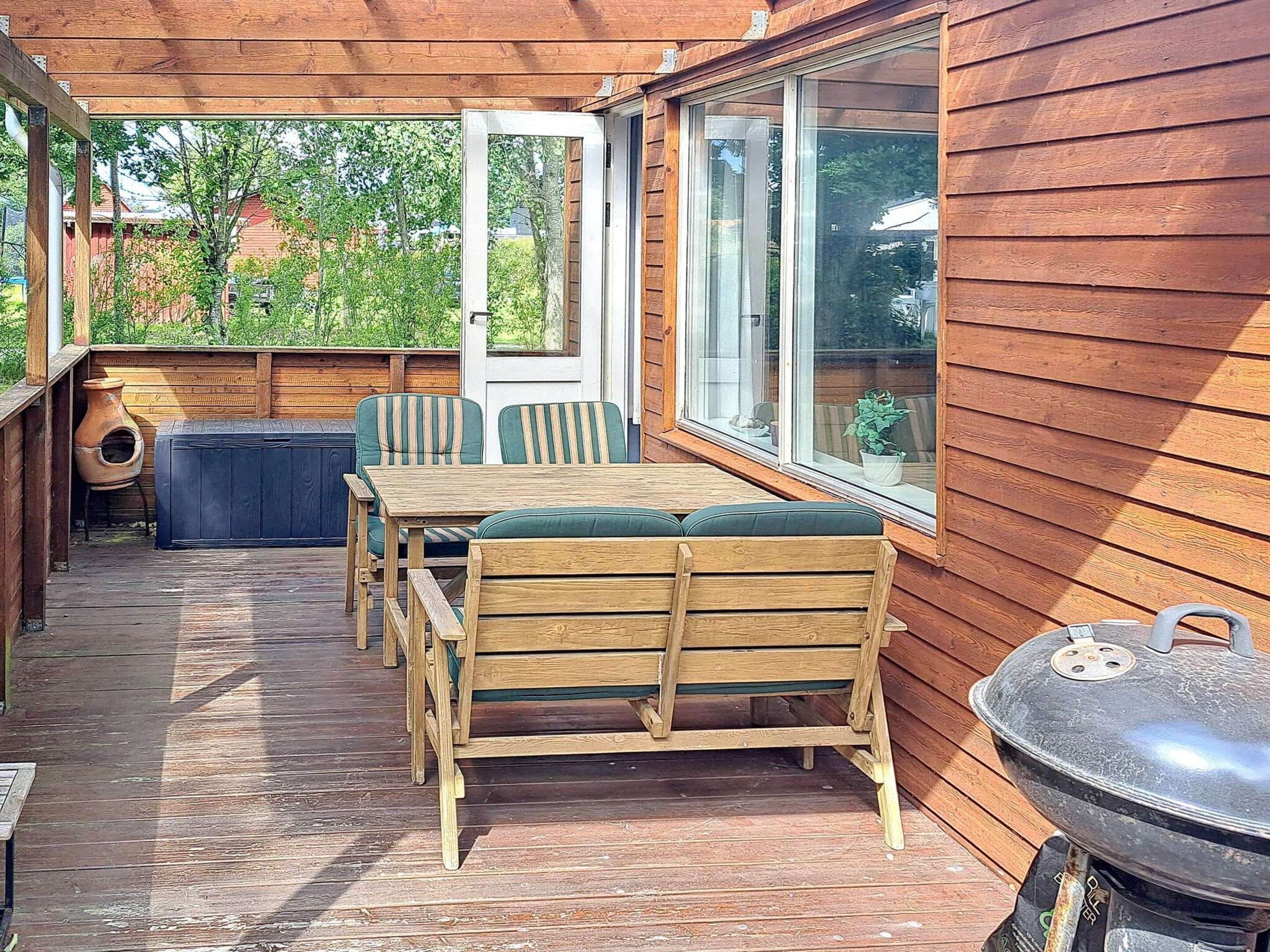 A wooden deck with a table and chairs, a barbecue grill, and a view of the surrounding area.