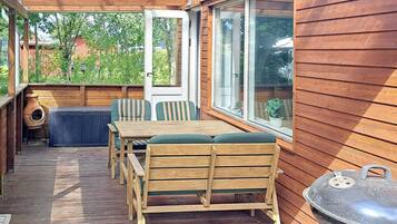 A wooden deck with a table and chairs, a barbecue grill, and a view of the surrounding area.