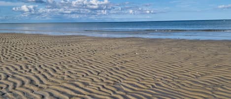 A sandy beach with visible footprints and a clear sky.