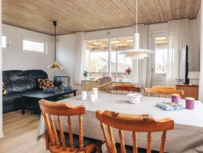 Una sala de estar moderna con techo de madera, un sofá de cuero negro, una mesa de comedor con sillas y ventanas amplias.