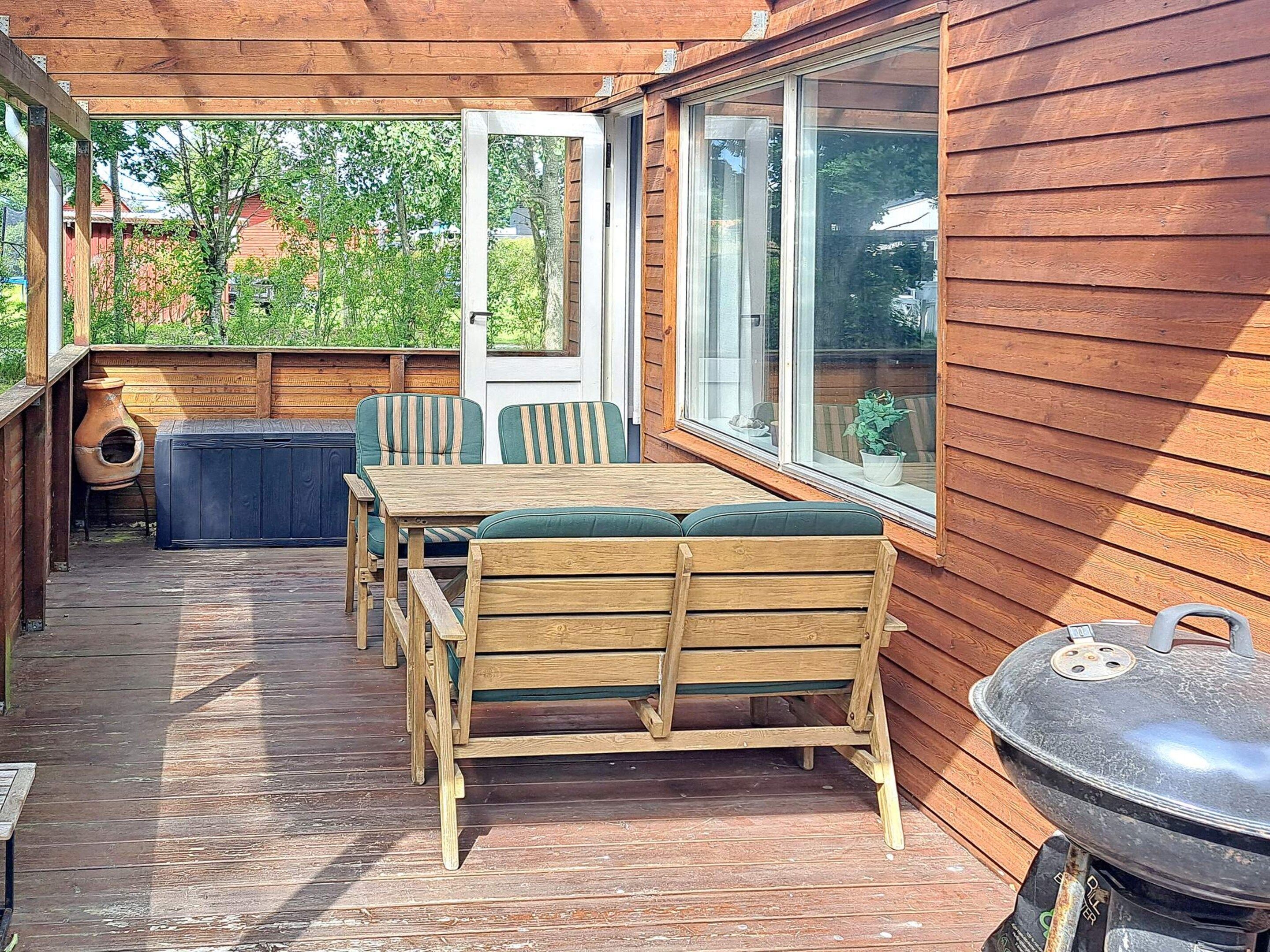 An outdoor patio with wooden furniture, a barbecue grill, and a view of the surrounding area.
