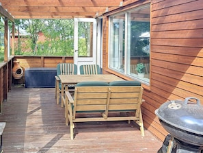 A wooden deck with a table and chairs, a barbecue grill, and a view of the surrounding area.