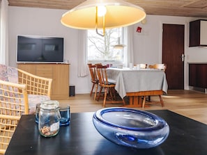 Un salon avec un tĂ©lĂ©viseur, des meubles en bois, une table Ă manger et une grande fenĂȘtre.