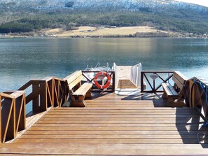 Un muelle de madera se extiende sobre aguas tranquilas, con un flotador y bancos.