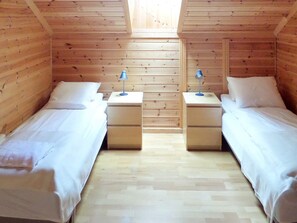 Una habitación con dos camas individuales, paredes de madera, techo inclinado y tragaluces.