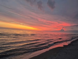 Uma praia com pôr do sol, ondas e céu limpo.