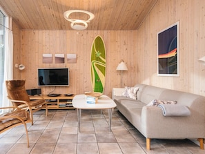 Uma sala de estar moderna com teto de madeira, televisão de tela plana, sofá, mesa de centro e decoração com prancha de surf.