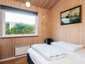 A bedroom with a large window, a bed with white bedding, a radiator, and a painting on the wall.