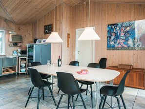 A modern kitchen with wooden walls, a dining area with a large table and chairs, and a painting on the wall. - 4 Star Holiday Home in Fano (Fano)
