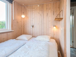 A room with two beds, wooden walls, a window, and a wall-mounted shelf. - 4 Star Holiday Home in Fano (Fano)