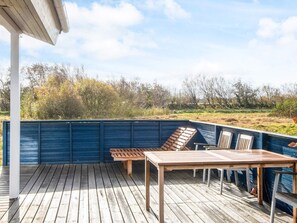 A wooden deck with a table and chairs, surrounded by a blue fence, overlooking a natural landscape.
