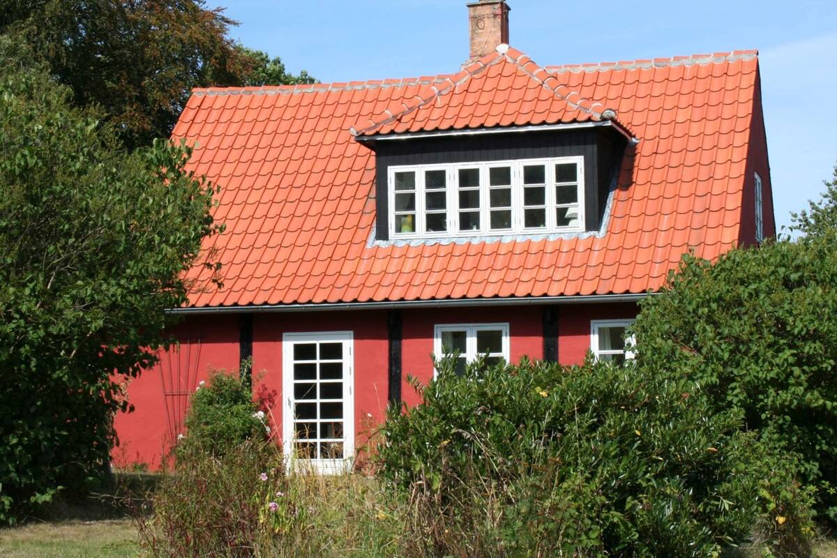 Et rødt hus med rødt tegltag, hvide vinduer og skorsten.