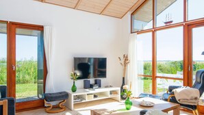 A spacious living room with a large TV, comfortable seating, a coffee table, and a view of greenery through large windows. - 8 Person Holiday Home in Ulfborg-by Traum (Ulfborg)