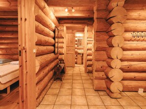 A log cabin interior with a central hallway, wooden walls, a bed, and a sink area.