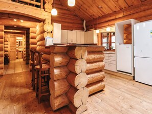 A log cabin interior with a central log structure, wooden floors, white cabinets, and a white refrigerator.